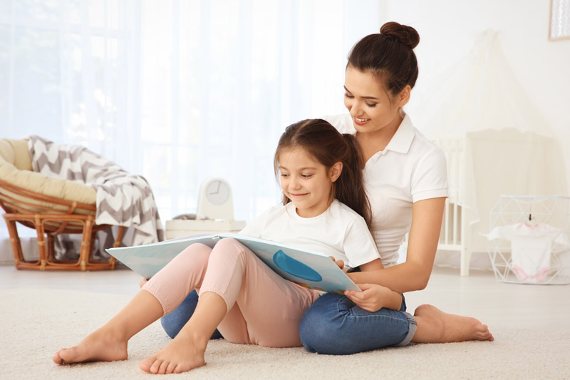 Mother and daughter sitting on carpet and reading a book