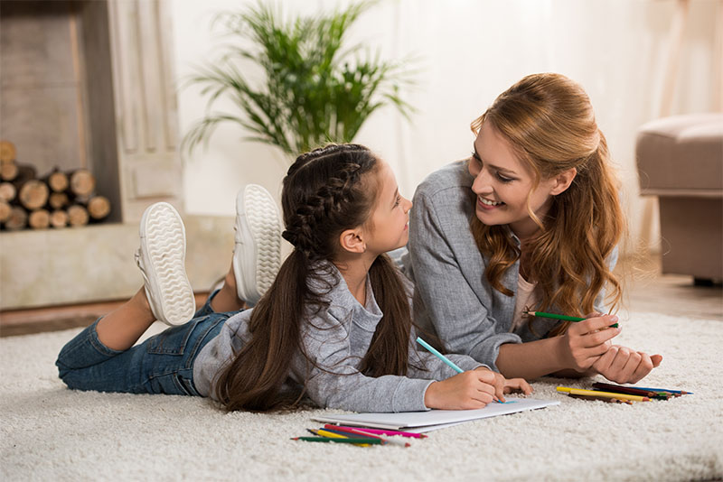 Mother and daughter lying on carpet and drawing